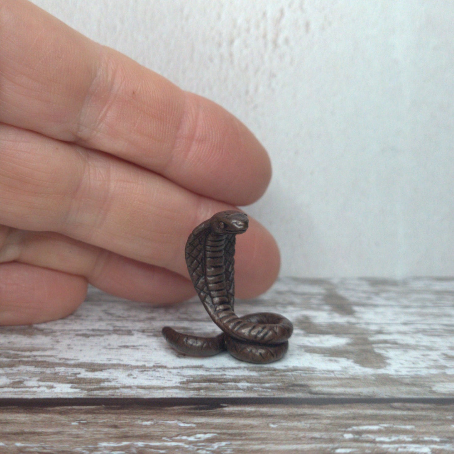 Miniature bronze cobra sculpture held between fingers to show scale, by David Meredith at Alcove Art
