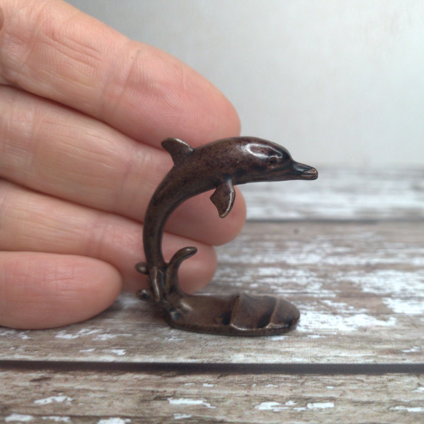 Miniature foundry-cast bronze leaping dolphin sculpture held in hand to show scale, by David Meredith at Alcove Art