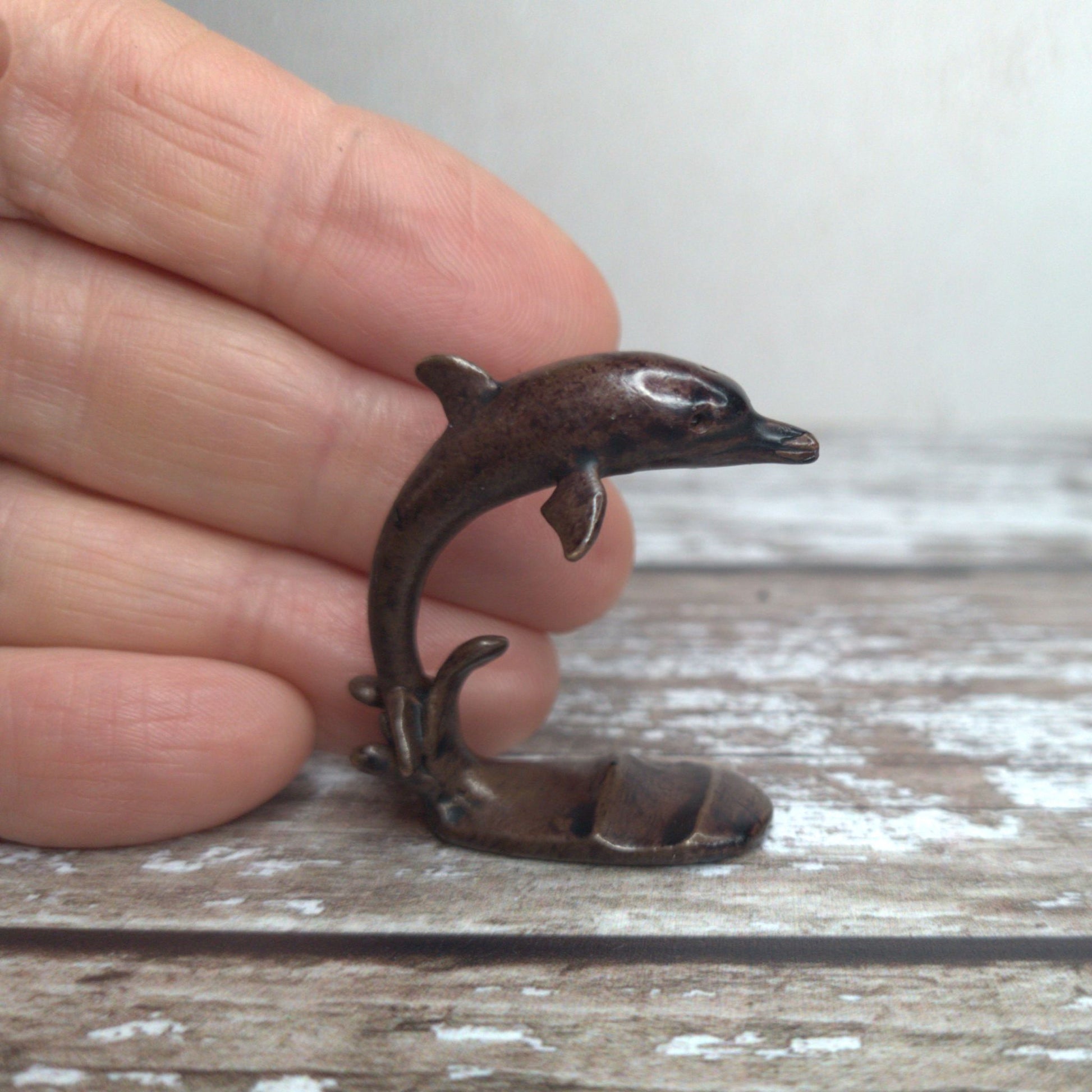 Miniature foundry-cast bronze leaping dolphin sculpture held in hand to show scale, by David Meredith at Alcove Art