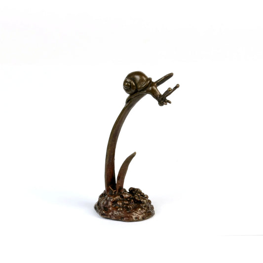 A miniature bronze snail perched on the end of an upright bronze leaf, facing right, against a white background
